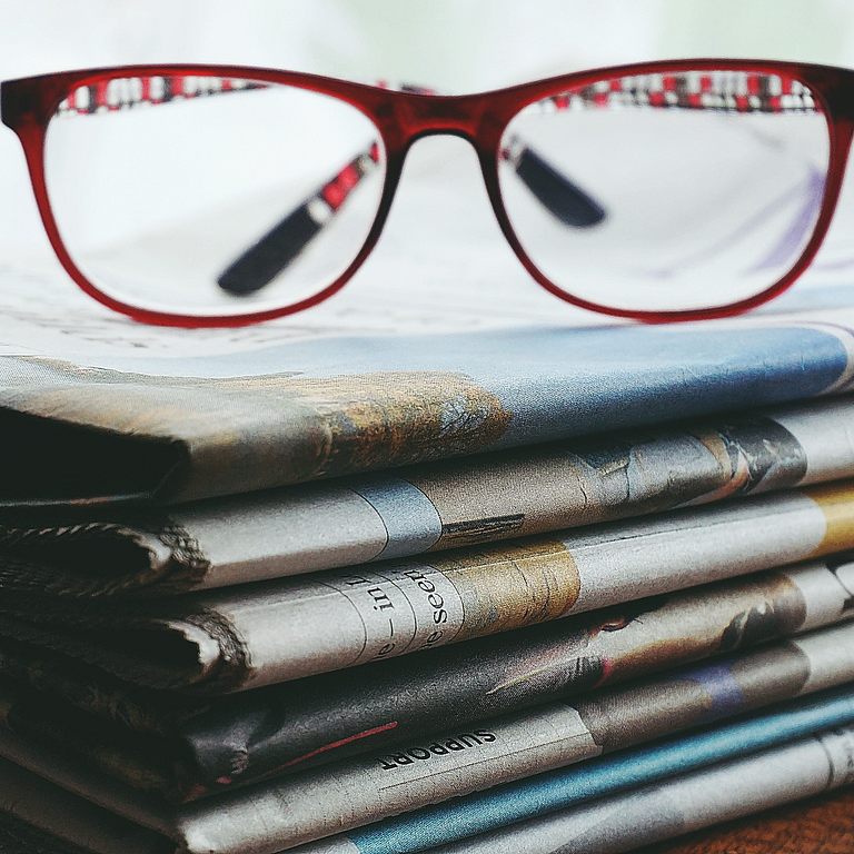 eine Brille liegt auf einem Zeitungsstapel