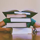 ein müder Student, der hinter seinem Bücherstapel ein Nickerchen macht