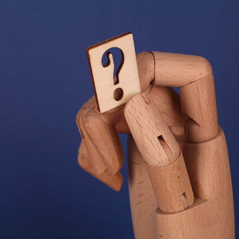 eine Holzhand hält ein Fragezeichen