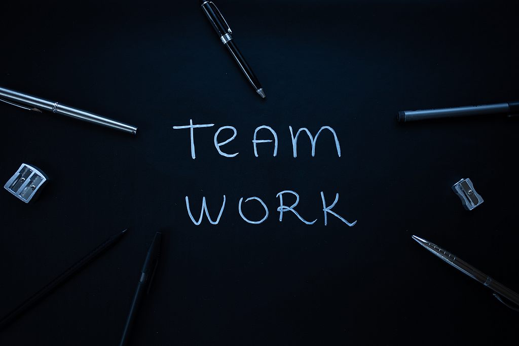 "Team work" steht auf einem Tisch geschrieben, auf dem Schreibmaterial herumliegt